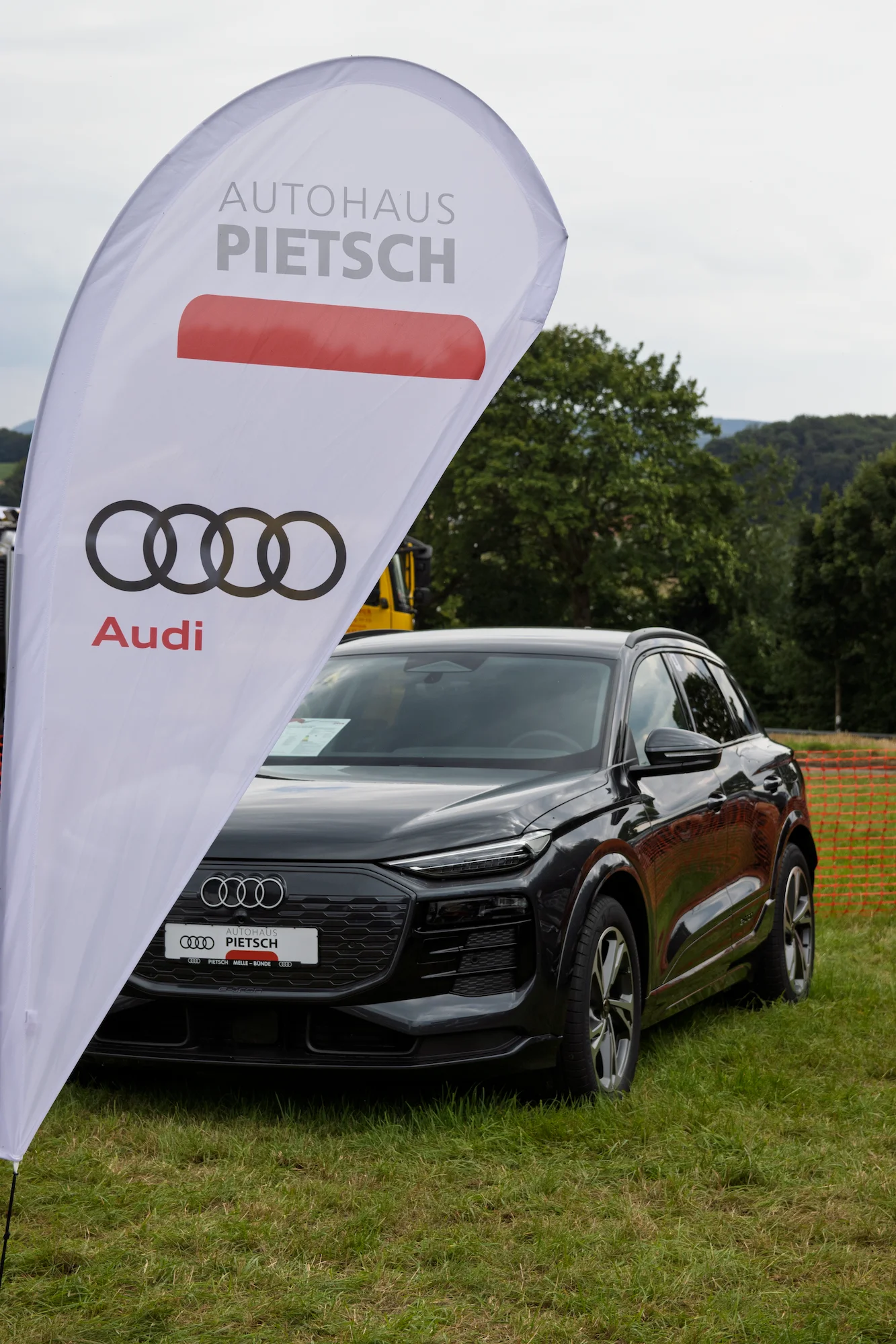 Audi Q6 e-tron in schwarz halbseitig, verdeckt von einem Pylon des Autohaus Pietsch von vorne aufgenommen
