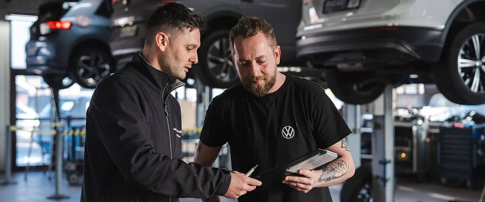 Zwei Mitarbeiter vom Autohaus Moser in der Werkstatt im Hintergrund stehen Fahrzeuge auf Hebebühnen