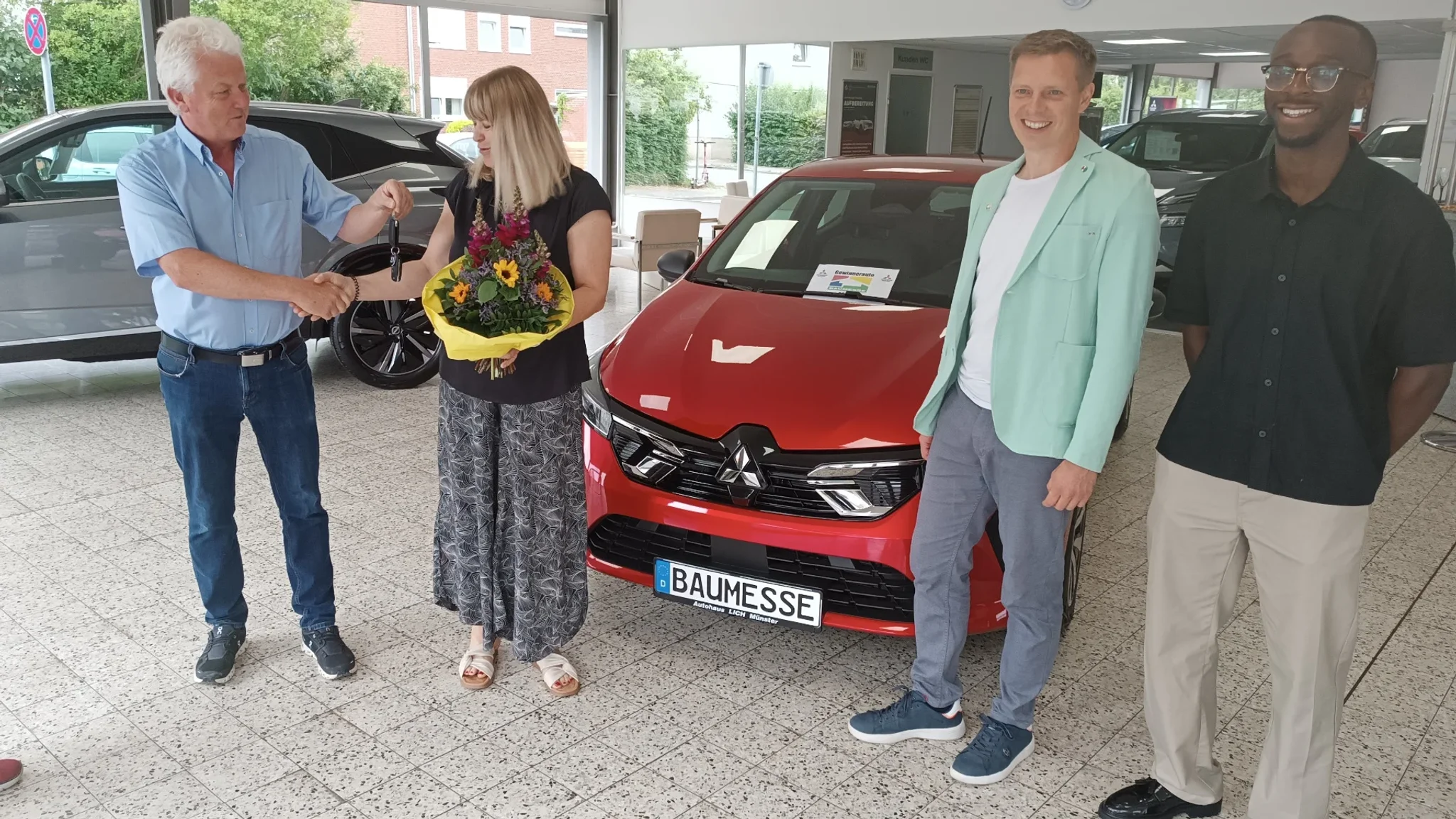 Mitarbeiter des Autohaus Lech und der Presse, zusammen mit der Gewinnerin vor einem roten Mitsubishi Colt