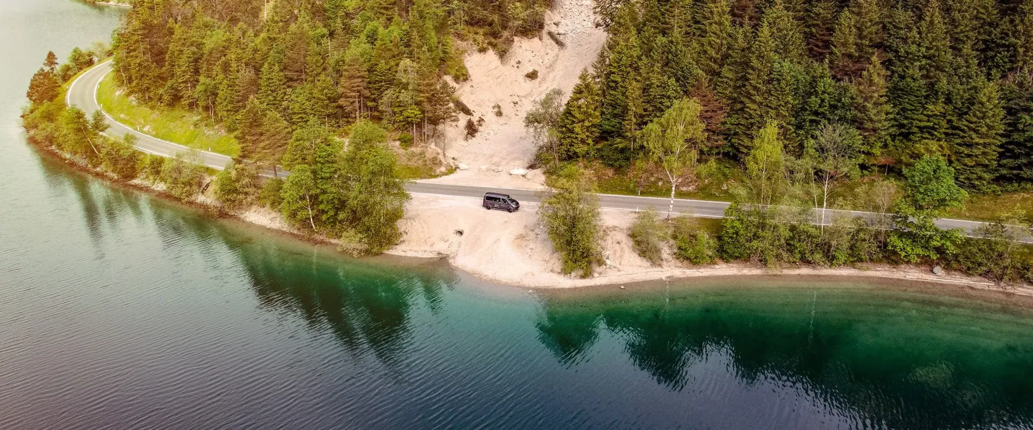 Bild eines VW-Bus von oben aufgenommen am Ufer eines Sees