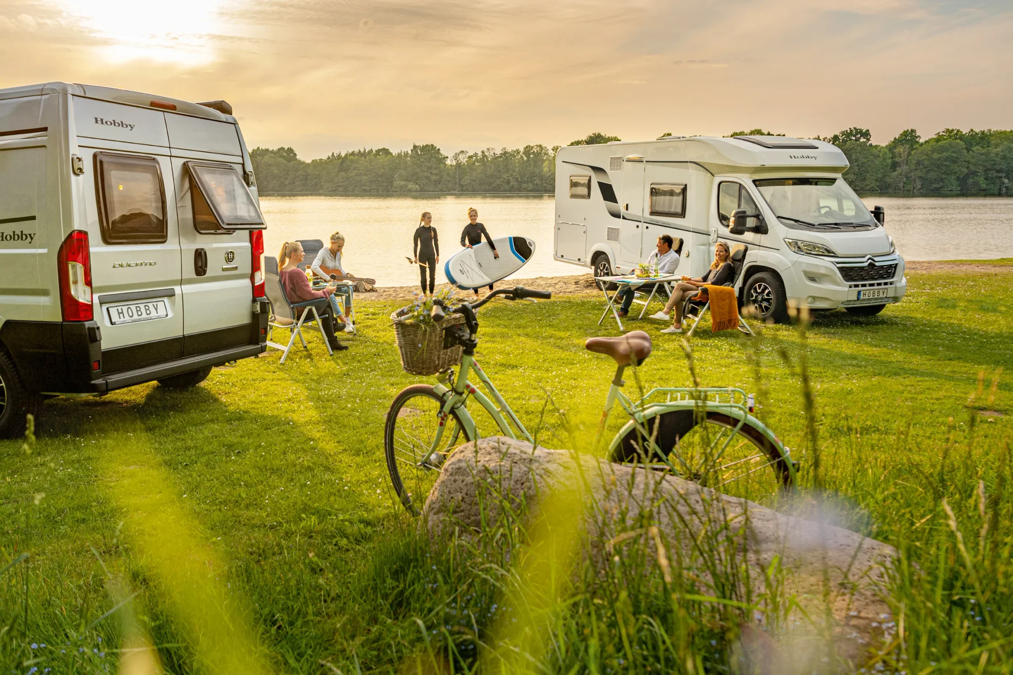 Hobby Reisemobile an einem See auf einer Wiese mit Personen