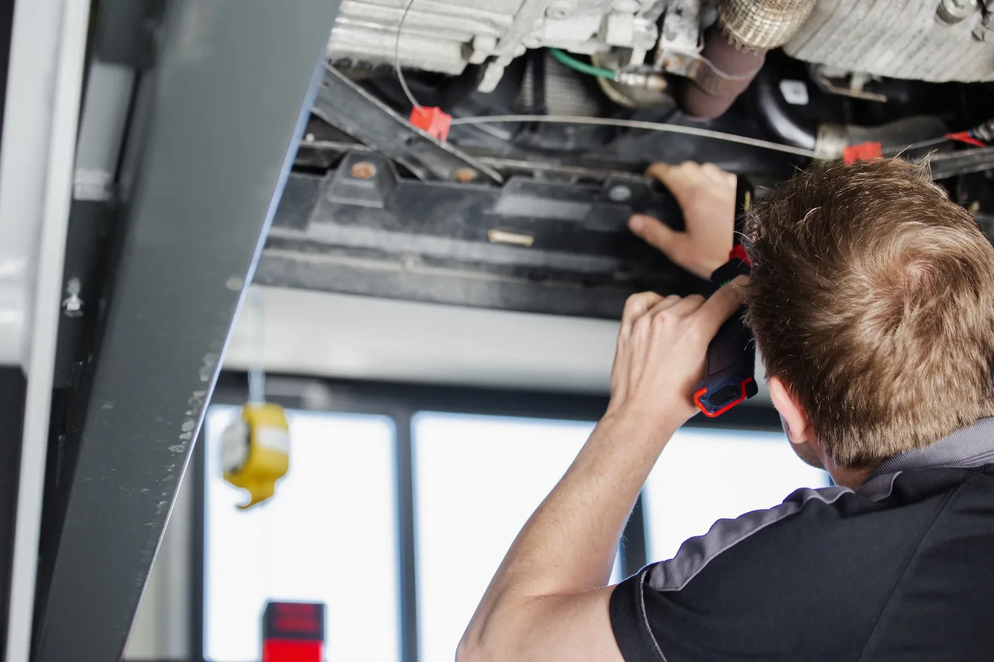 Mechaniker am Autohaus Hager und Penzel bei Instandsetzungsarbeiten am Fahrzeugunterboden. Das Fahrzeug steht auf einer Hebebühne.