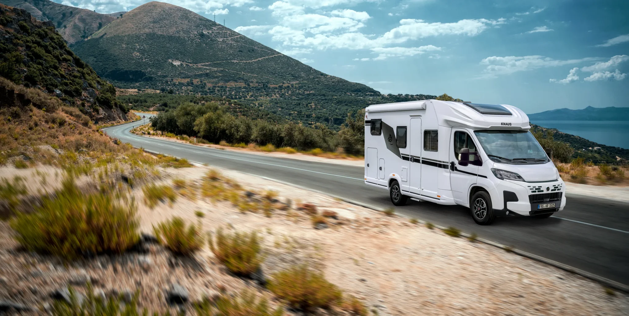 Weißes Knaus Wohnmobil das auf einer mediterranen Straße fährt 