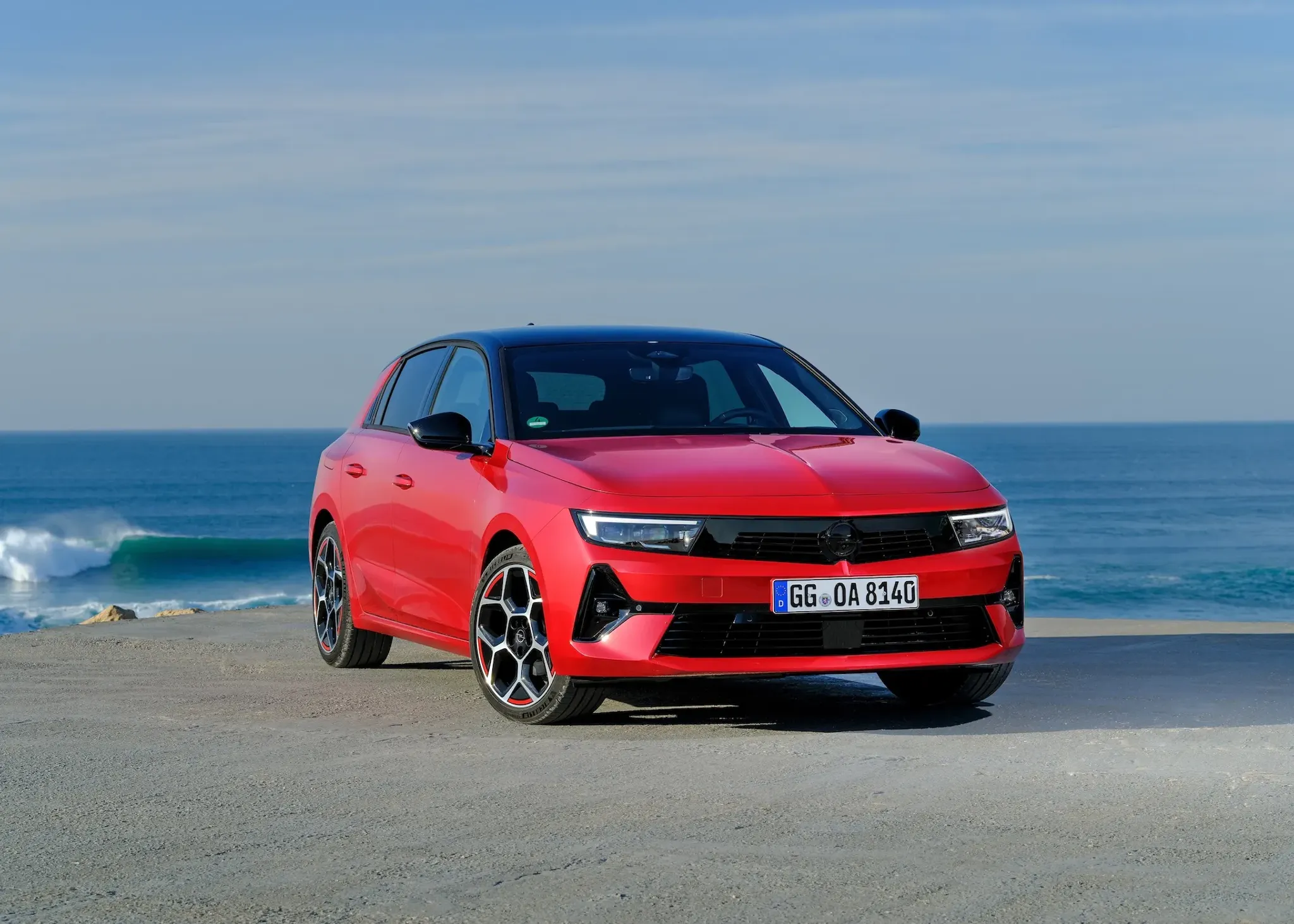 Opel Astra in Rot am Strand vor blauem Meer fotografiert von vorne rechts