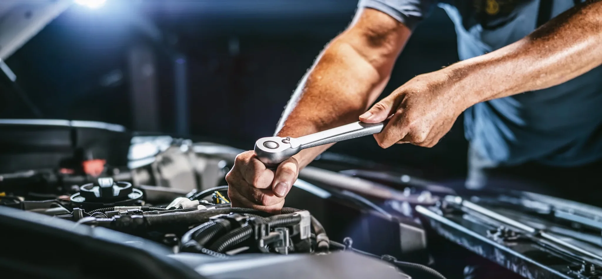 Mechaniker mit Schraubenschlüssel im Motorraum eines Fahrzeugs
