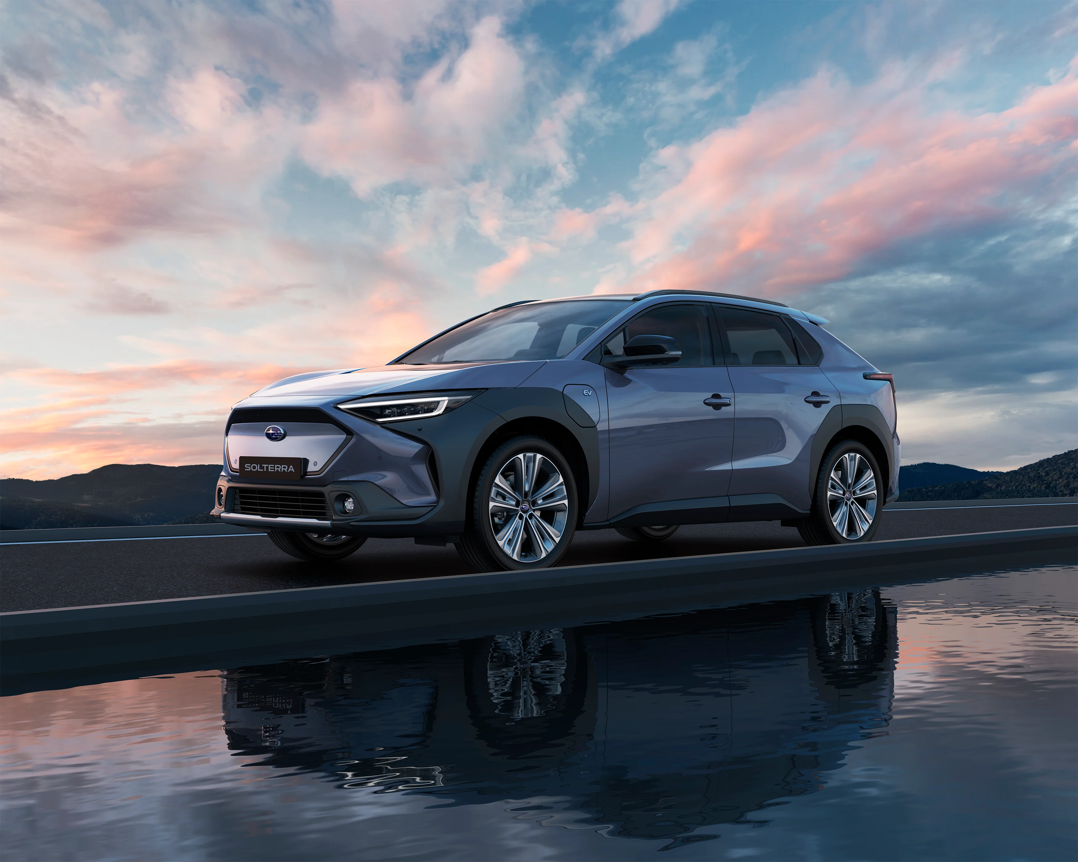 Blauer Subaru Solterra steht bei Sonnenuntergang auf Straße mit Wasserreflexion.