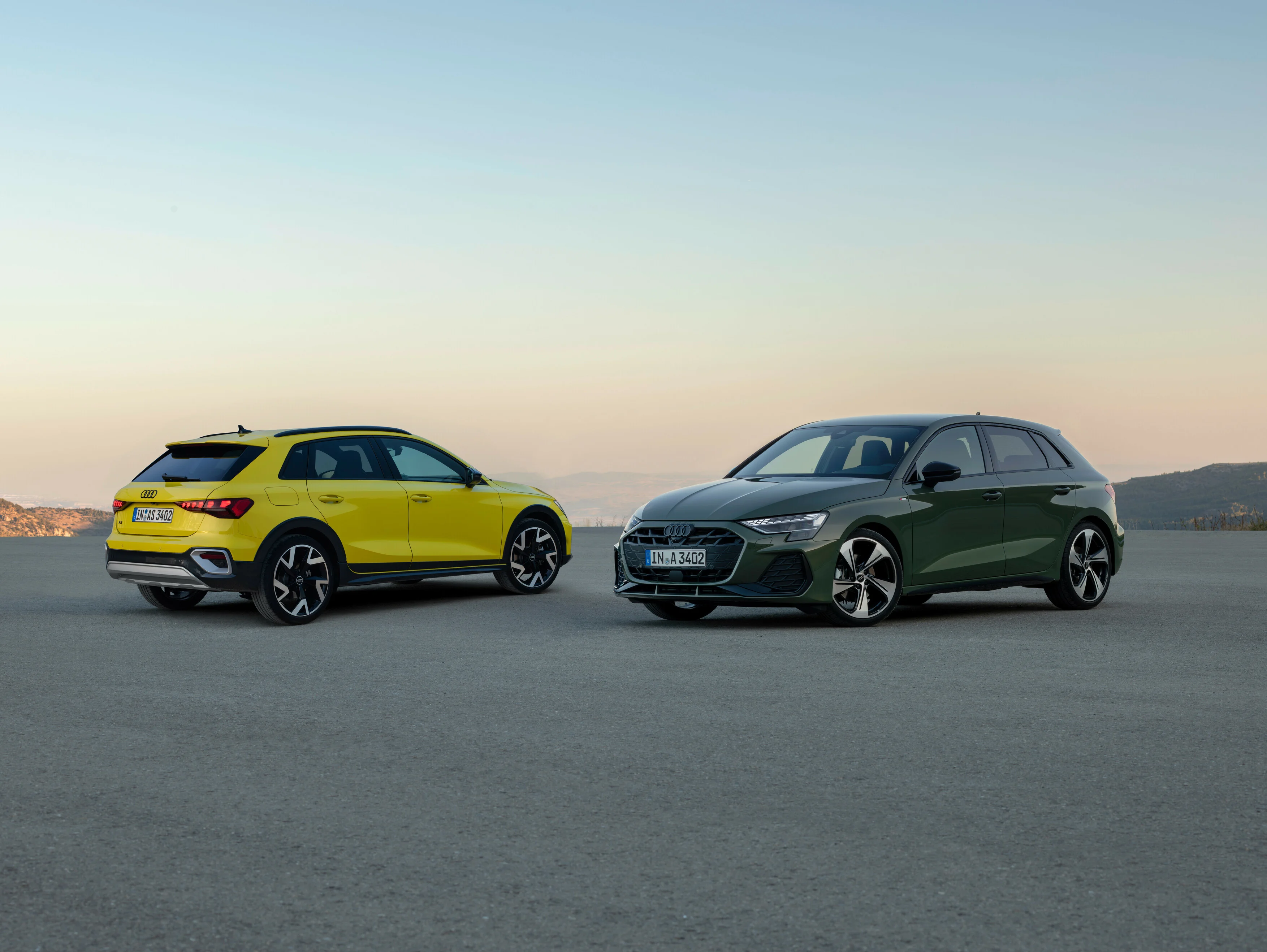 Der Audi A3 allstreet in Pythongelb und Audi A3 Sportback in Distriktgrün Metallic als Standaufnahme mit Panoramaausblick bei Sonnenuntergang.
