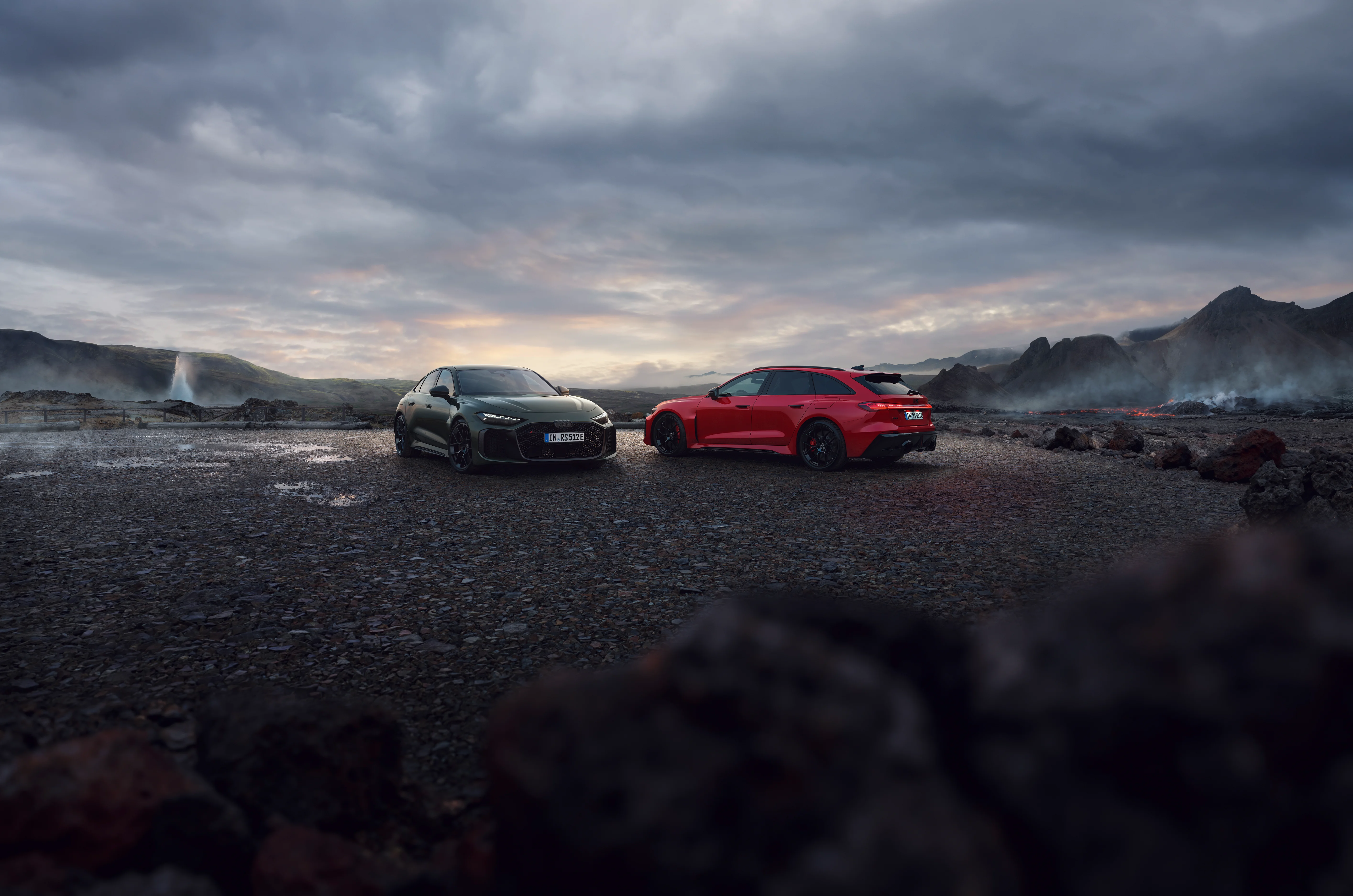 Audi RS 5 Avant in rot und Limousine in grün auf Schotterplatz im Nebel und Sonnenuntergang im Bergpanorama.