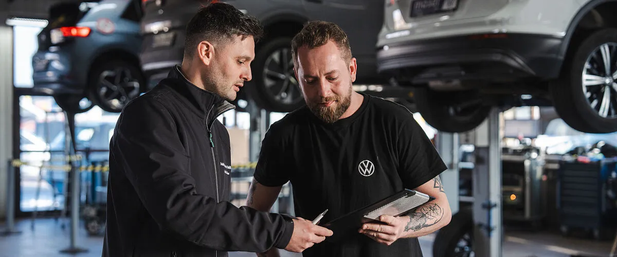 Zwei Mitarbeiter vom Autohaus Moser in der Werkstatt im Hintergrund stehen Fahrzeuge auf Hebebühnen