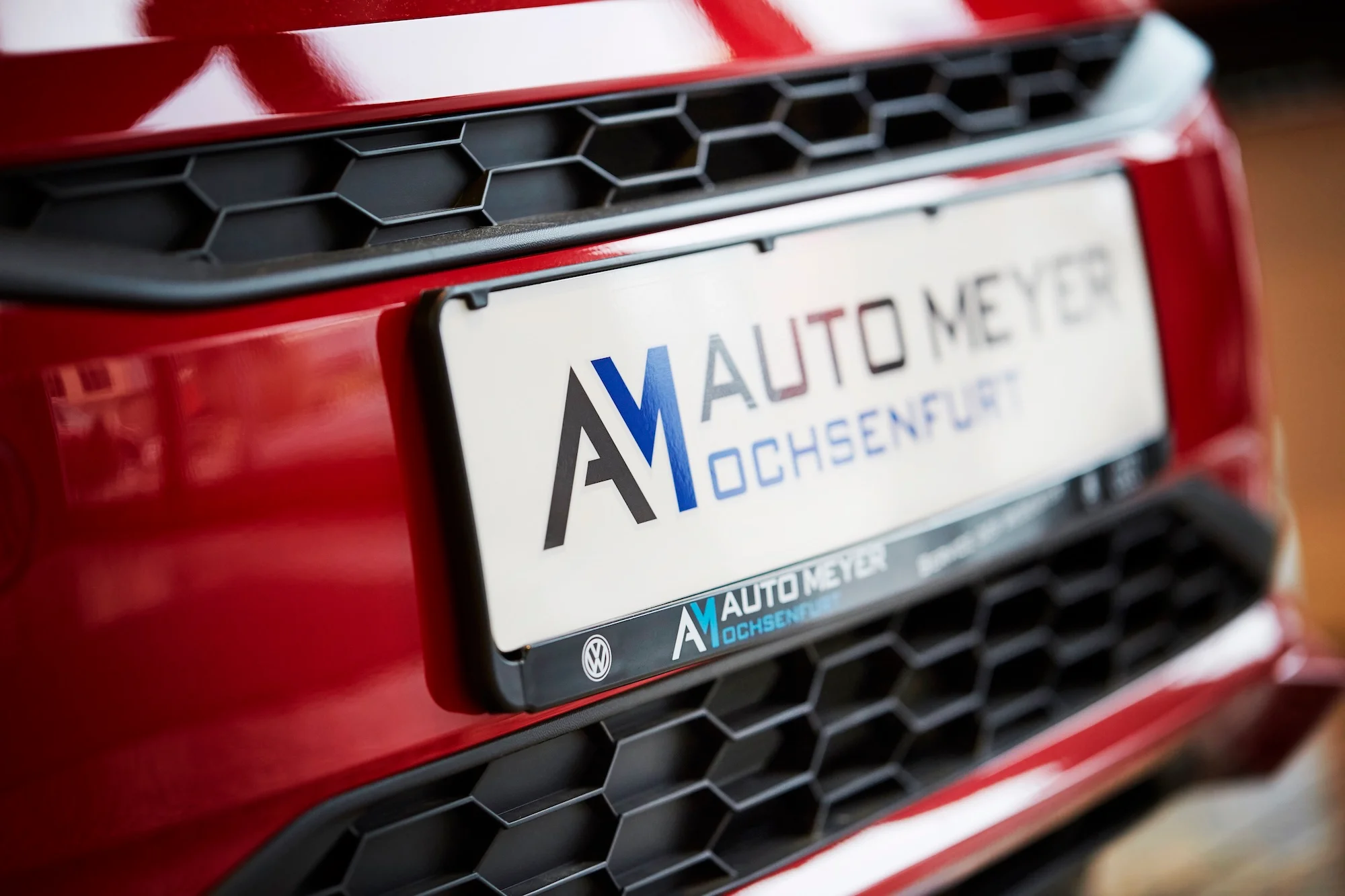 Detailaufnahme eines Kühlergrill eines Volkswagen mit Kennzeicheneinleger Auto Meyer das Fahrzeug hat eine rote Lackierung