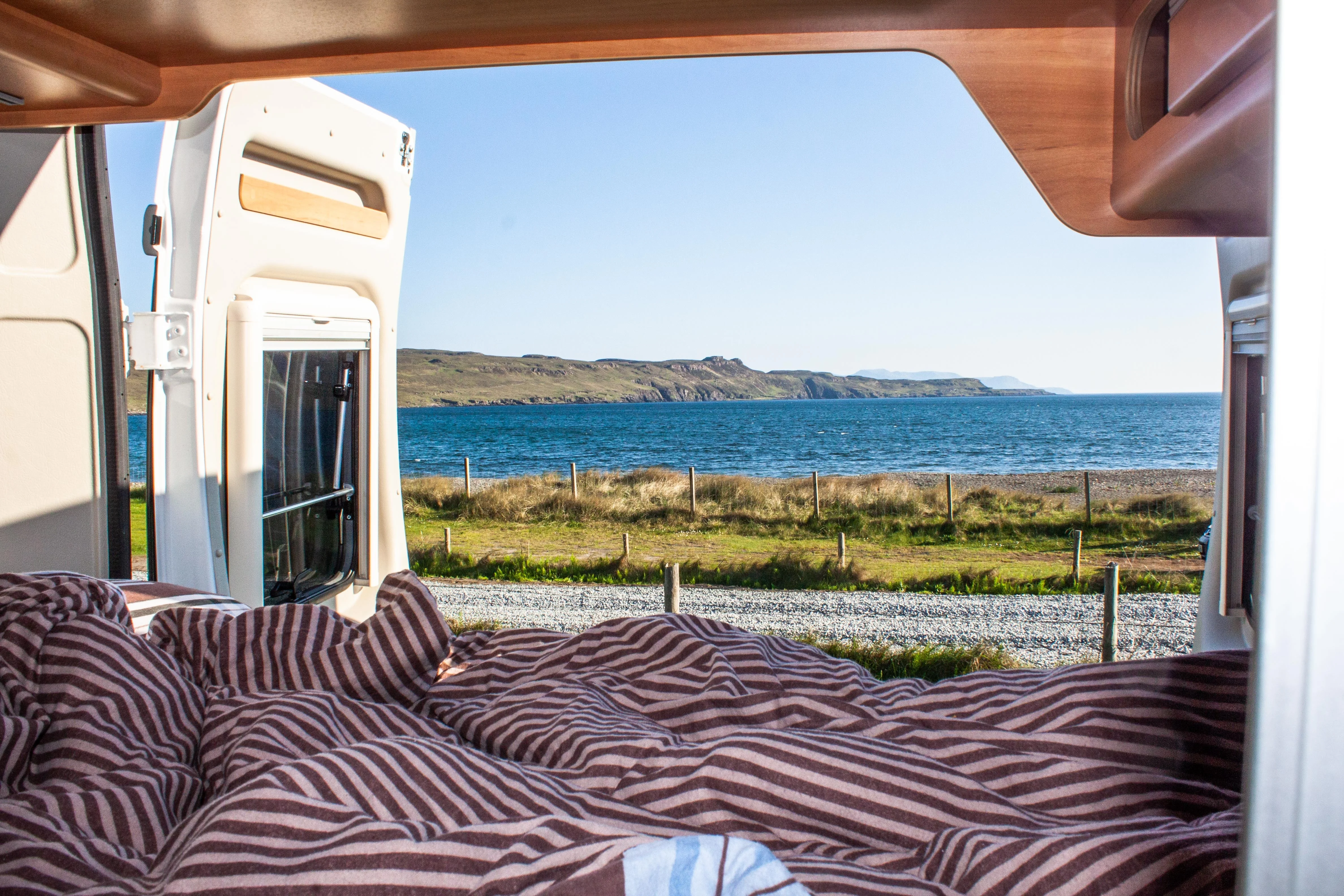 Camper Van mit offener Hecktür mit Blick auf Sand und Meer