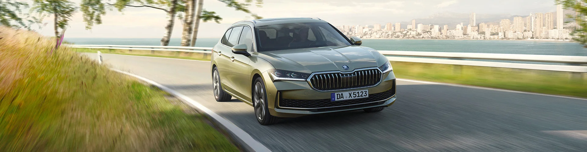 Skoda Superb auf einer kurvigen Straße mit Meer und Skyline im Hintergrund