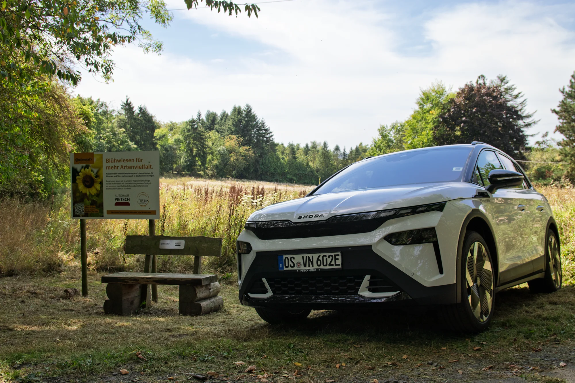 Skoda Elroq neben Bank und Infotafel vor der Blühwiese