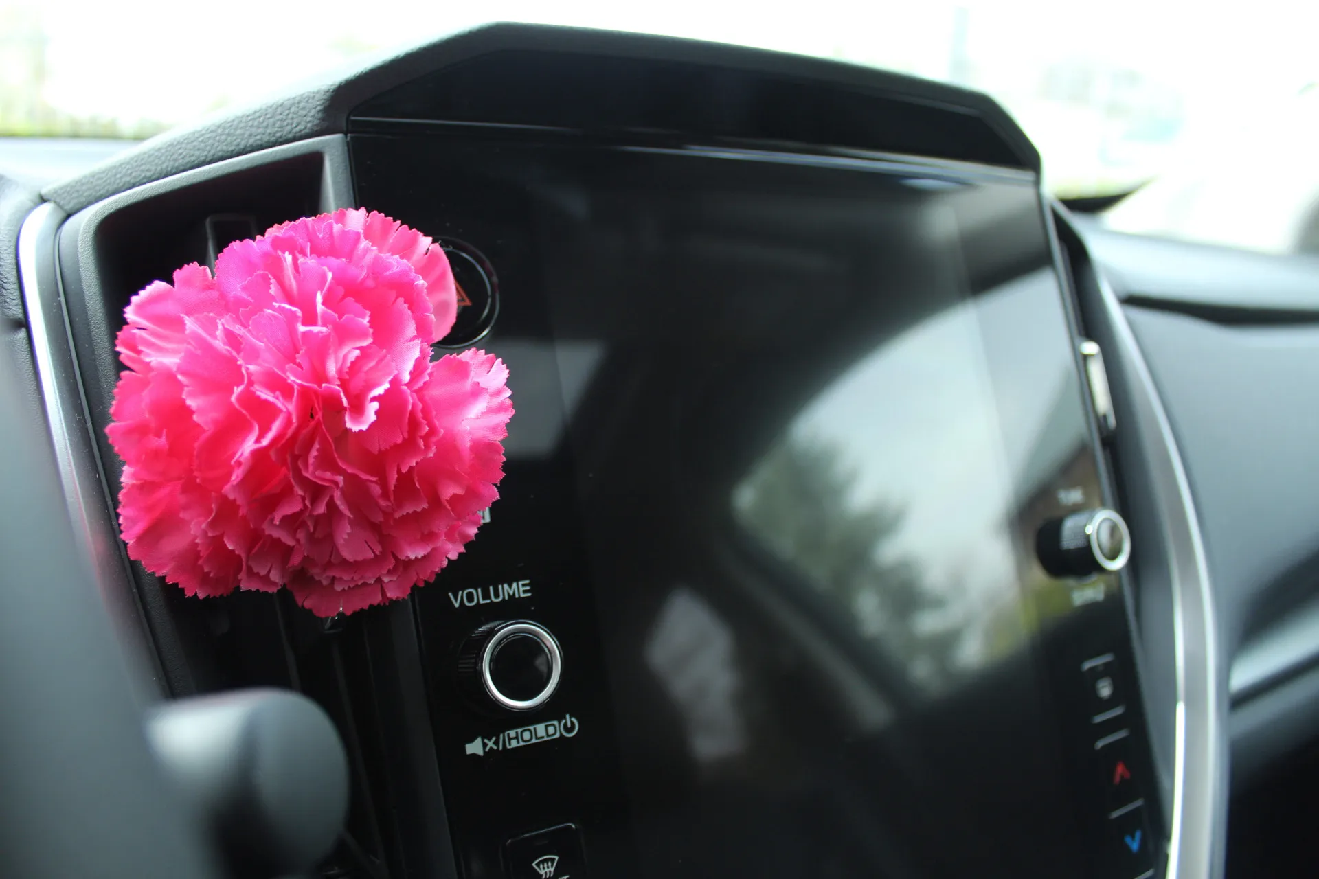 Pinkfarbene künstliche Blume am Lautstärkeregler eines Fahrzeugdisplays befestigt.