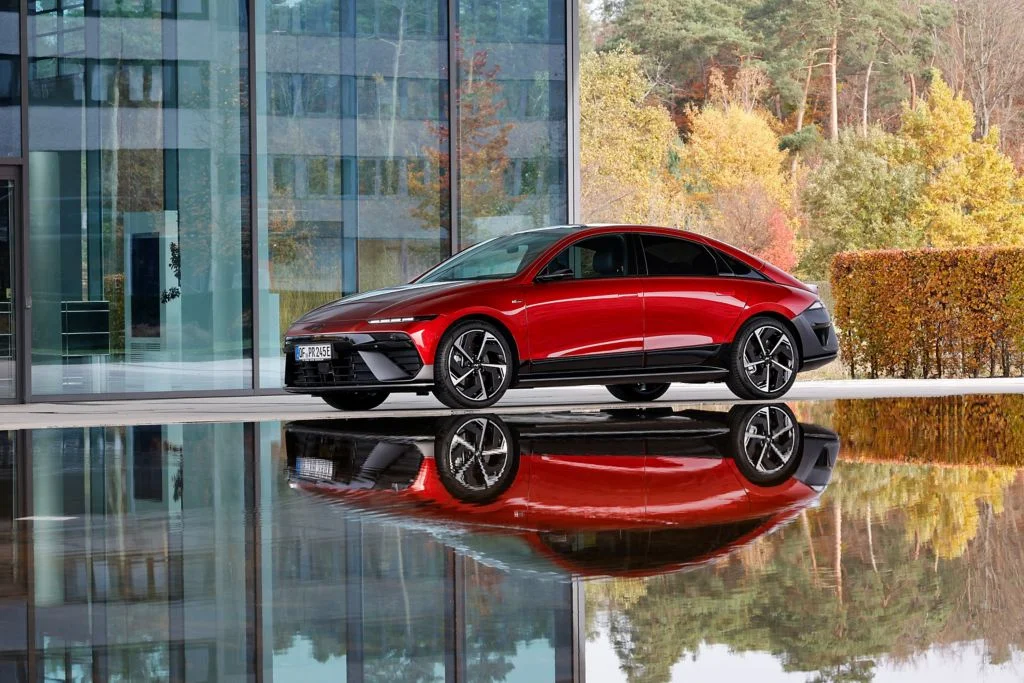 Hyundai Ioniq 6, in rot stehend, vor einem Gebäude an einem künstlichen Teich