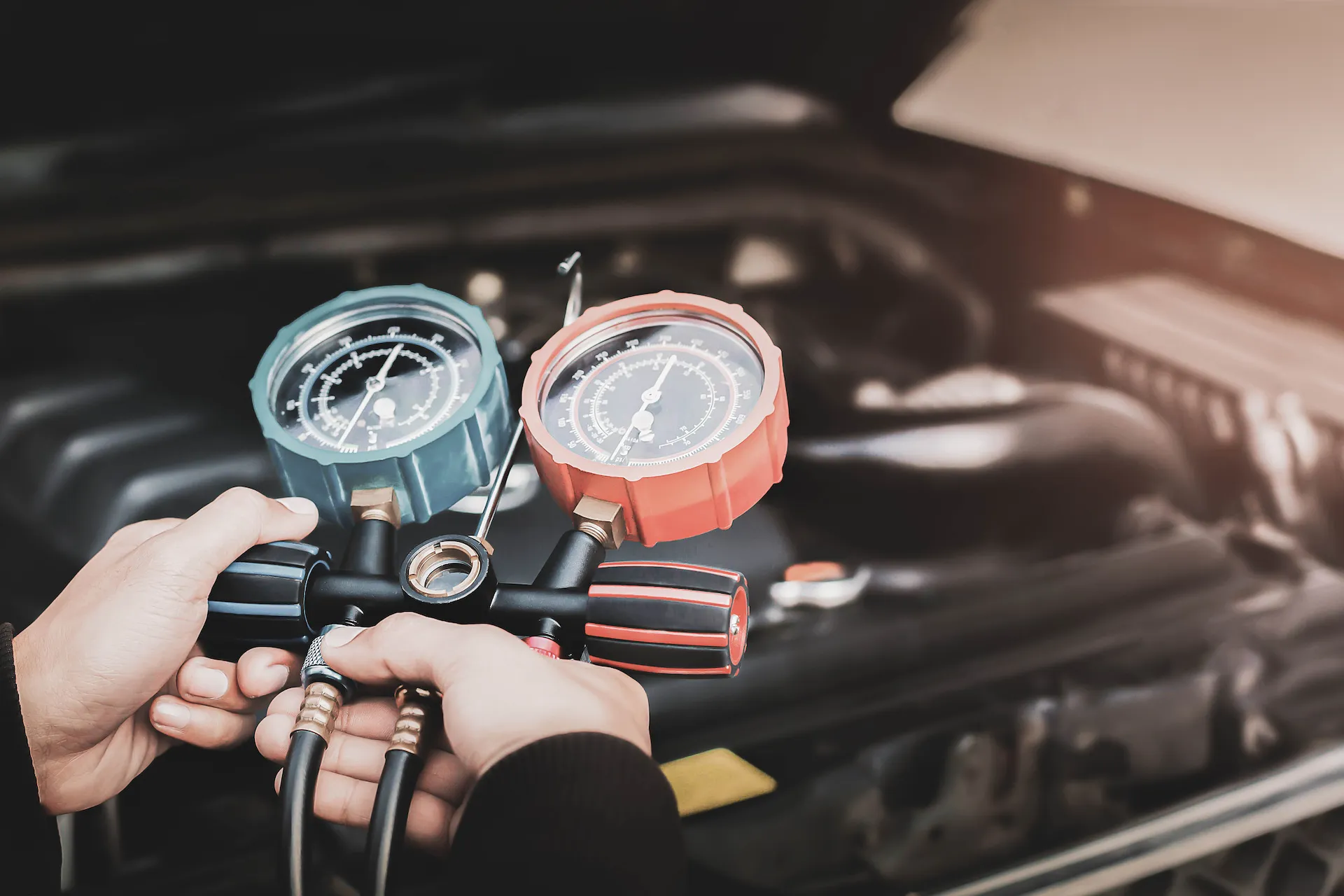 Fahrzeug mit geöffneter Motorhaube ein Mitarbeiter prüft mittels Manometer den Druck der Klimaanlage