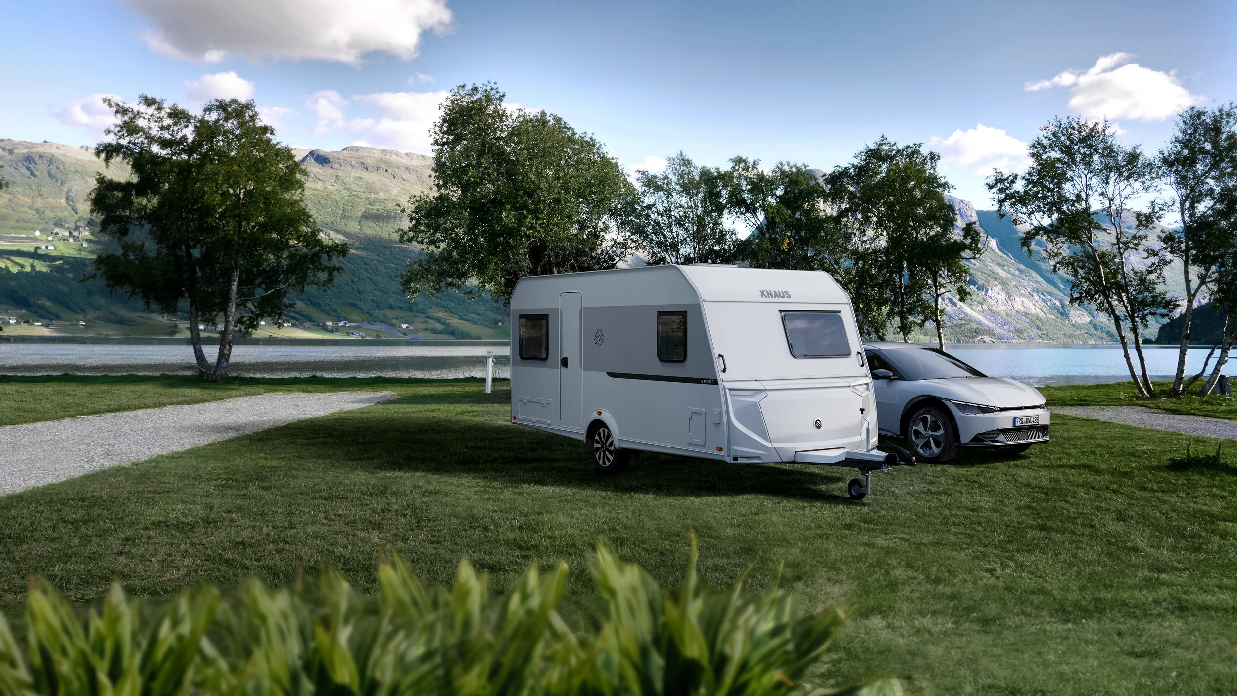 Knaus Sport Wohnwagen auf einer Wiese mit einem See und Bergen im Hintergrund