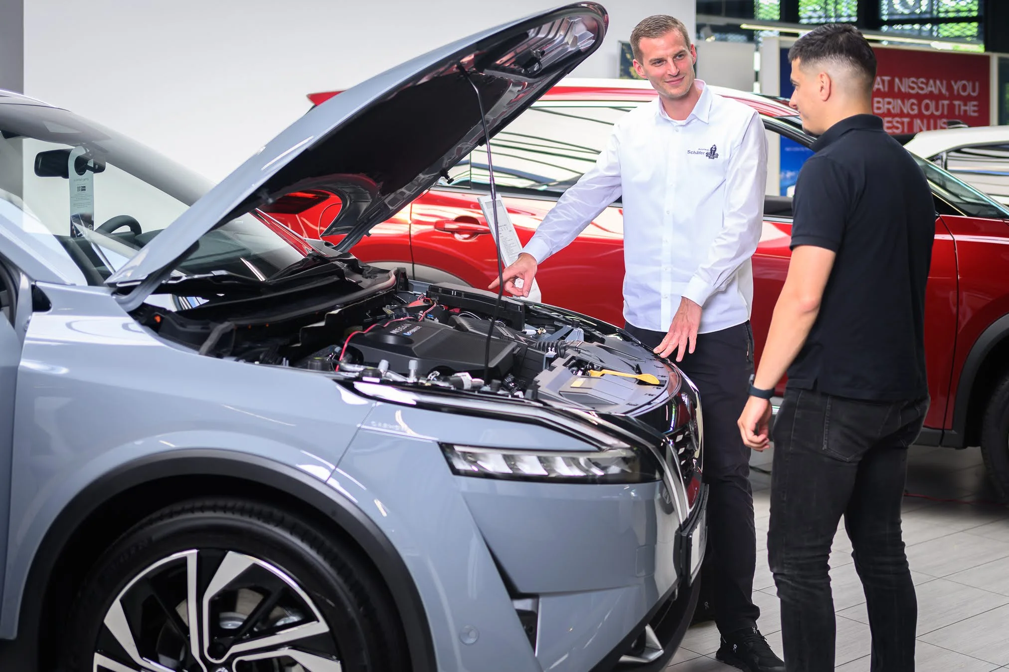 Serviceberater mit Kunden an einem Fahrzeug mit geöffneter Motorhaube