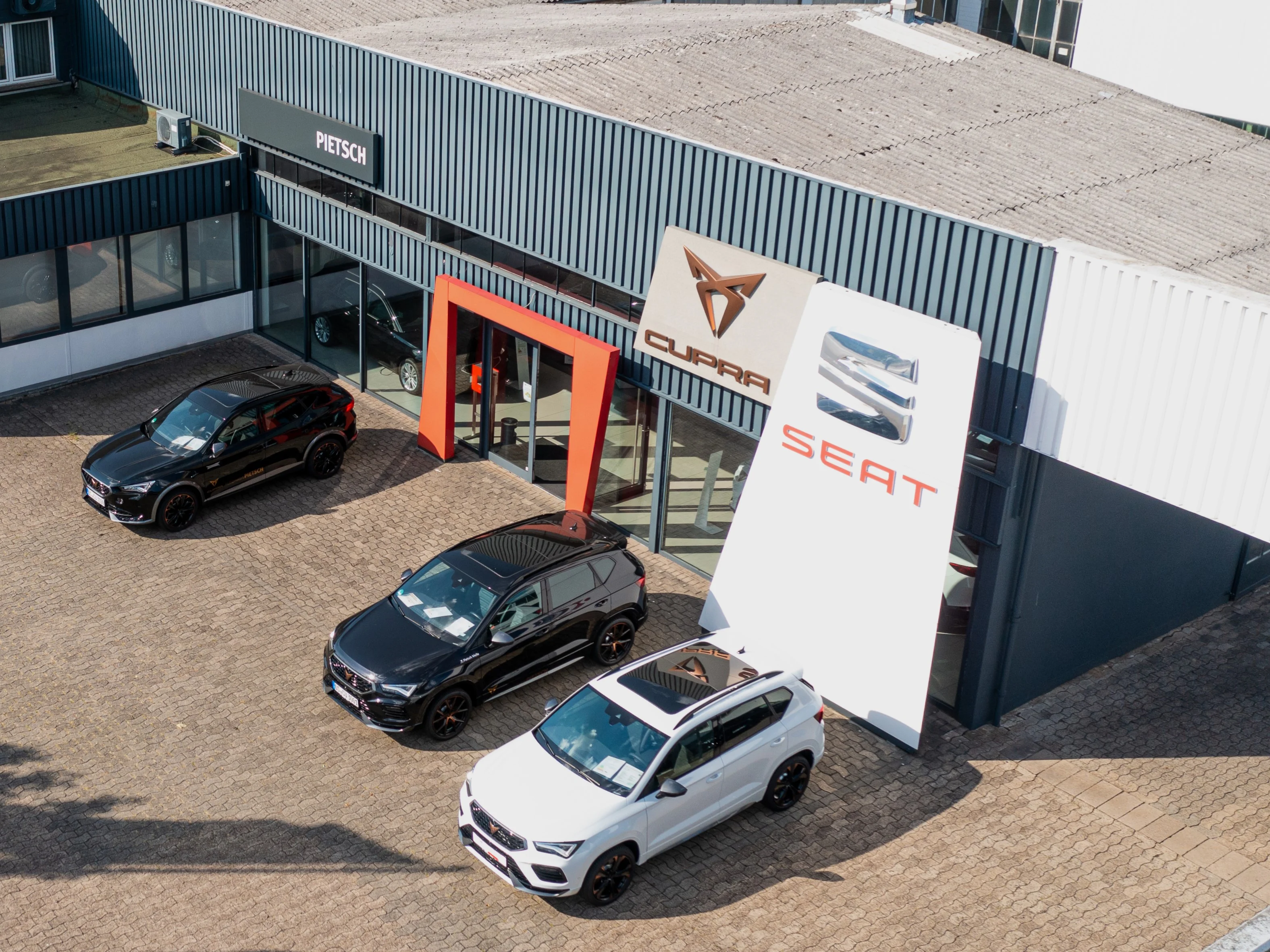 Luftaufnahme der Seat und Cupra Ausstellungshalle mit Blick auf den Eingang und geparkten Vorführwagen vor der Halle