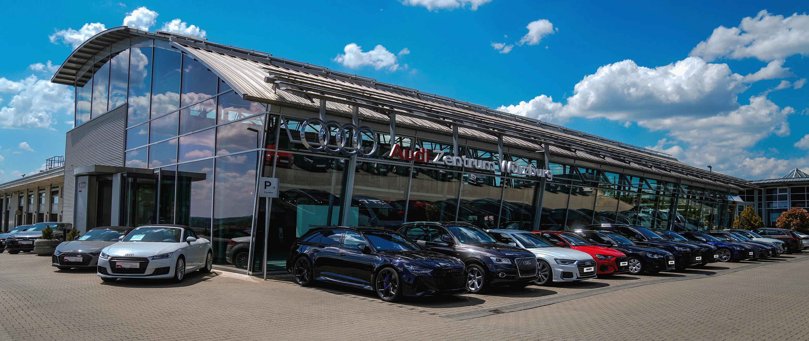 Außenaufnahme des Spindler Audi Zentrum Würzburg mit geparkten Fahrzeugen vor der Glasfassade