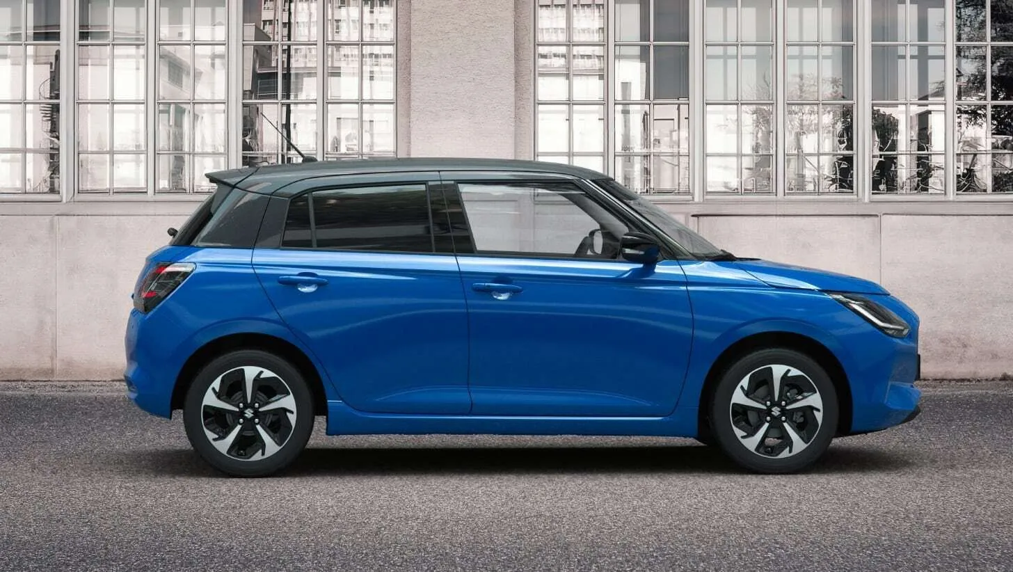 Der neue Suzuki swift in blau mit Anthrazitfarbe im Dach in der Seitenansicht vor einem Lagergebäude
