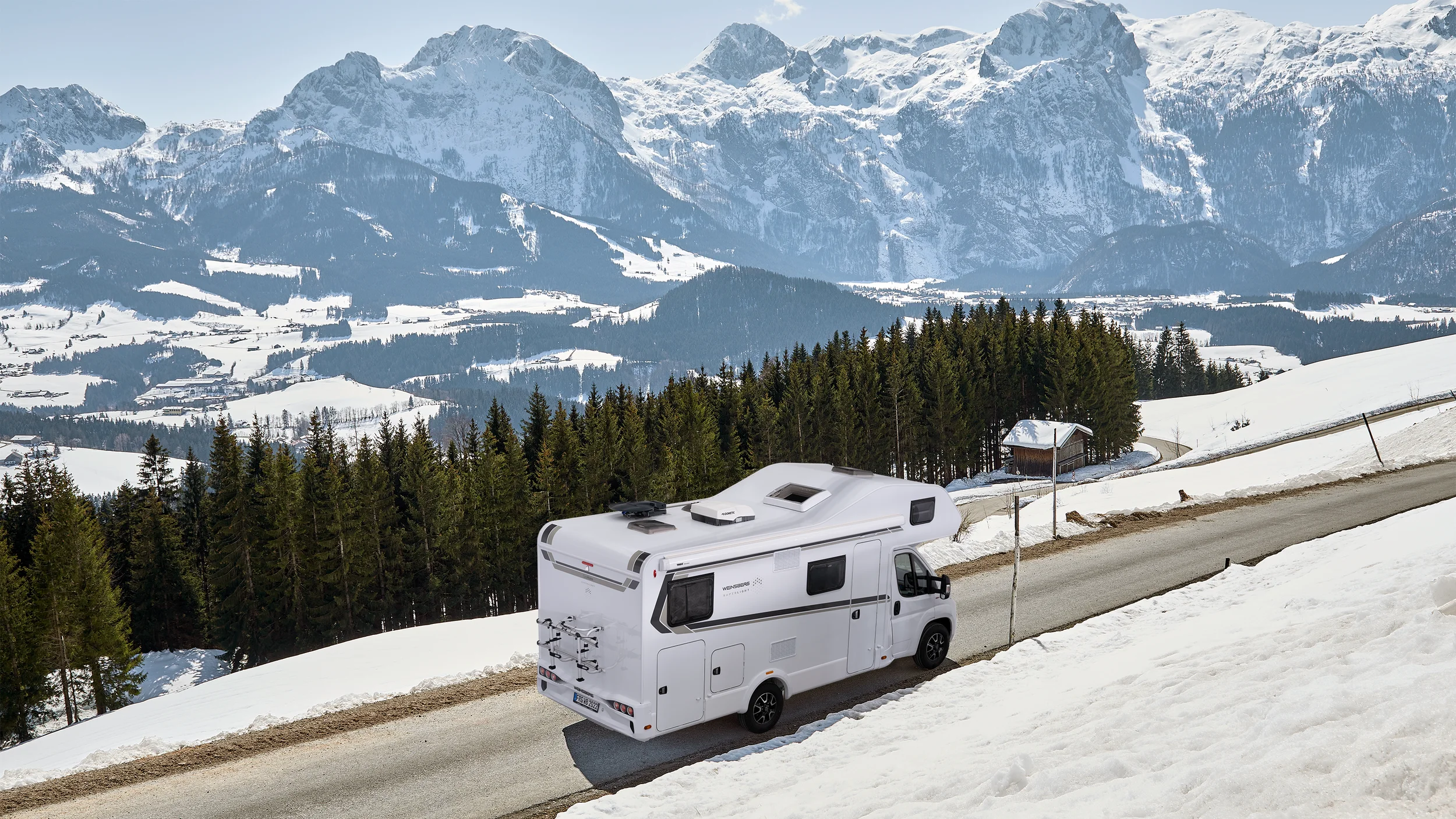Wohnmobil fährt im Winter durch verschneite Berglandschaft – Weinsberg Alkoven-Modell auf Panoramastraße mit Alpenblick.